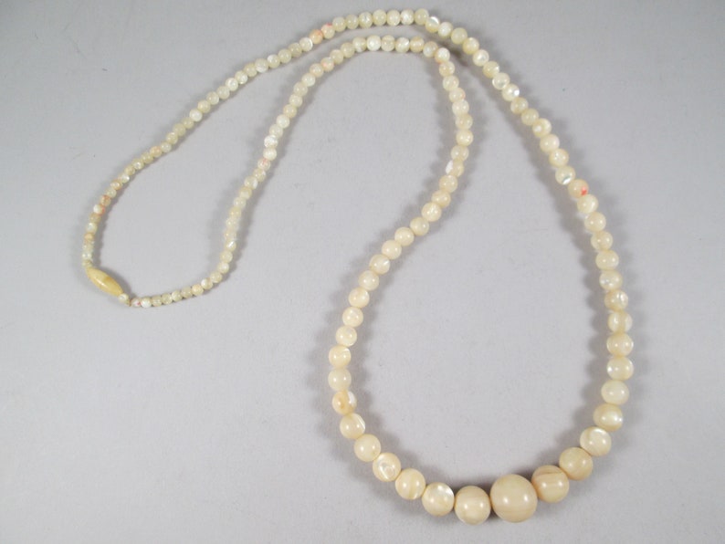 May include: A long white pearl necklace with a single larger pearl at the center.