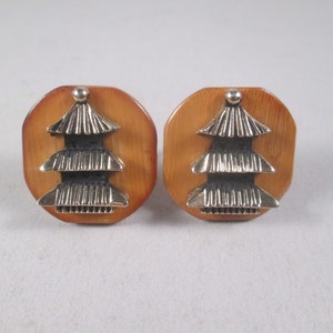 Può includere: Un paio di gemelli con un design a pagoda dorata su sfondo marrone.