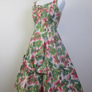 Op de afbeelding: Een vintage jurk met bloemenprint, een sweetheart-halslijn en een volle rok. De jurk is gemaakt van een lichtgewicht stof en heeft een groen, roze en wit bloemenpatroon.
