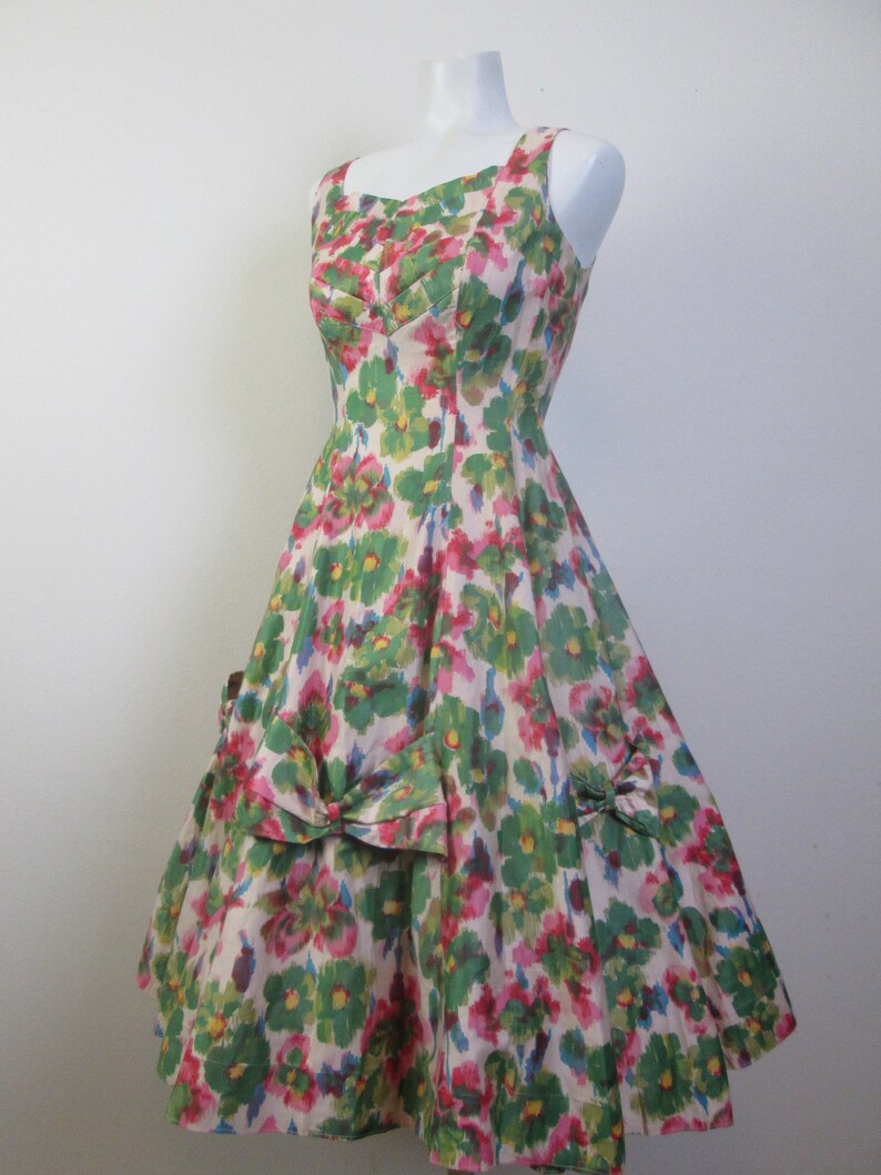 Op de afbeelding: Een vintage jurk met bloemenprint, een sweetheart-halslijn en een volle rok. De jurk is gemaakt van een lichtgewicht stof en heeft een groen, roze en wit bloemenpatroon.