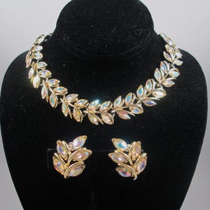 Peut inclure: Un collier et des boucles d'oreilles en ton or avec des strass irisés en forme de feuilles.