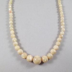 May include: A white pearl necklace with a larger pearl in the center.