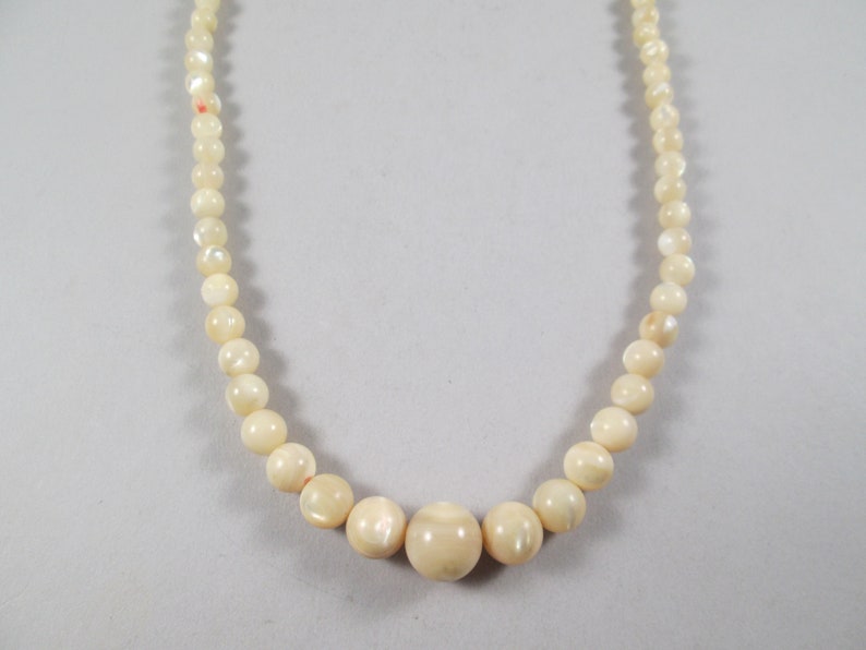 May include: A white pearl necklace with a larger pearl in the center.