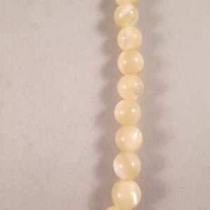 May include: A strand of white pearl-like beads. The beads are round and have a slight iridescent sheen.