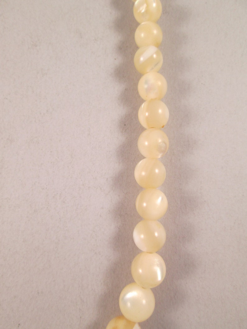 May include: A strand of white pearl-like beads. The beads are round and have a slight iridescent sheen.