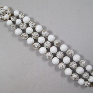 May include: A white and gray beaded bracelet with a gold clasp. The beads are round and have a speckled pattern.