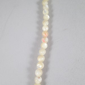 May include: A strand of white pearl beads with iridescent shimmer.