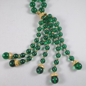 Pu&ograve; includere: Una lunga collana di perline di vetro verde smeraldo con un pendente di perline pi&ugrave; piccole. La collana ha una chiusura dorata e dettagli dorati sulle perline.