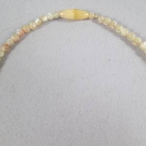 May include: A white and cream colored beaded necklace with a larger, oval-shaped bead in the center.