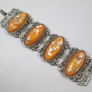 May include: A silver bracelet with four oval-shaped orange and white stones set in ornate silver frames.