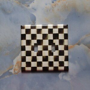May include: A white and black checkered light switch cover plate. The plate has a distressed look and is made of plastic.