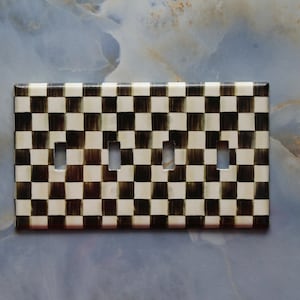 May include: A black and white checkered light switch cover plate with four cutouts for light switches.