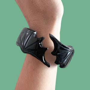 May include: A black plastic bracelet with a geometric design. The bracelet is broken in two pieces.