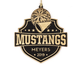 May include: Wooden ornament with a shield design. The ornament features the word "MUSTANGS" in a bold font, along with "MEYERS" and the year "2019". A cheerleader's megaphone and pom-pom are also depicted.