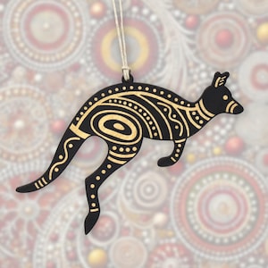 May include: A black kangaroo ornament with gold-colored decorative patterns. The kangaroo is suspended by a natural-colored string. The background features a blurred pattern of circular designs in various colors, creating a festive or artistic feel.