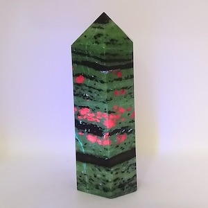 May include: A green, black and red crystal point with a pointed top and a hexagonal base.