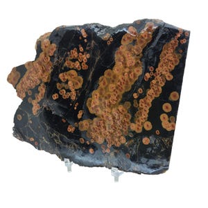 May include: A large, irregularly shaped slab of black and orange jasper with a swirling pattern of orange and red spots. The jasper is polished and has a smooth surface.