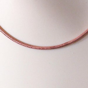 May include: A rose gold snake chain necklace. The chain is made of small, tightly woven links.