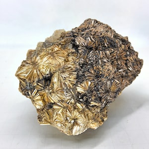 Puede incluir: Un cúmulo de cristales de color marrón dorado con una superficie rugosa y texturizada. Los cristales están dispuestos en un patrón de estrella, creando una muestra visualmente atractiva y única.