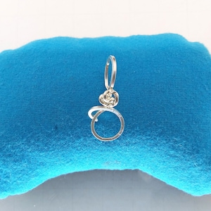 May include: A silver wire pendant with a circle and a knot design. The pendant is on a blue background.