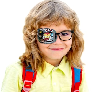 May include: A child wearing glasses with a colorful eye patch featuring cartoon superheroes. The eye patch is gray with a white border and has a variety of cartoon characters including Iron Man, Captain America, and Spider-Man. The child is wearing a yellow polo shirt and a red backpack.