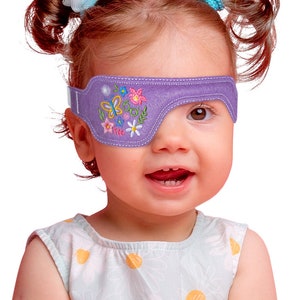 May include: A purple eye patch with embroidered flowers and butterflies. The patch is worn by a young child with brown hair and a light blue and yellow floral dress.