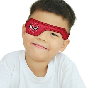 May include: A red eye patch with a white embroidered Spiderman design. The eye patch is worn by a young boy with short black hair.