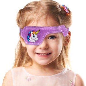 May include: A purple eye patch with a white unicorn embroidered on it. The unicorn has a rainbow mane and a yellow horn. The eye patch is worn by a young girl with blonde hair.