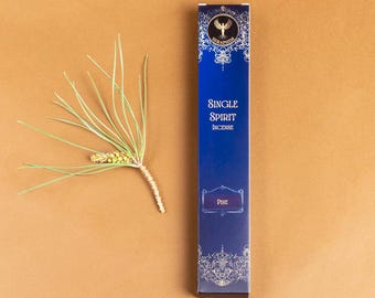 May include: A navy blue incense box with gold and white decorative elements and the text "SINGLE SPIRIT INCENSE". A sprig of pine needles and a pine cone are to the left of the box. The box reads "PINE".