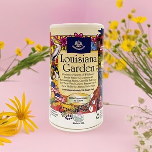 May include: A colorful can of Louisiana Garden wildflower seeds. The can features a whimsical illustration of a Louisiana scene with a pelican, a crawfish, and a fleur-de-lis. The text on the can reads "Louisiana Garden" and "Contains a Variety of Wildflower Seeds Native to Louisiana & Surrounding States, Carefully Selected for Their Vivid Colors, Fragrances & Their Ability to Attract Butterflies. Covers Approximately 100 Square Feet. 100% Guaranteed to Grow."