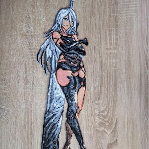 Puede incluir: Una figura de arte de píxeles de una mujer con cabello largo y blanco, vestida con un atuendo negro y sosteniendo una espada grande. La figura está hecha de pequeñas cuentas de colores y está sobre un fondo de madera.