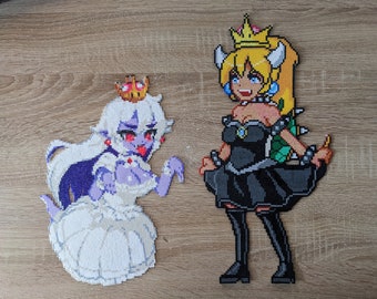 May include: Two pixel art figures of Princess Peach and Bowser Jr. made with perler beads. Princess Peach is wearing a white dress and a crown. Bowser Jr. is wearing a black dress and a crown.