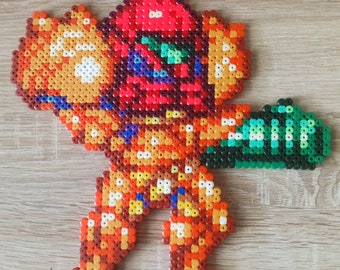 May include: A pixel art character made of colourful beads, depicting a video game character wearing a red helmet and holding a green weapon.