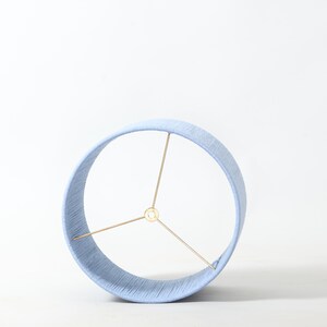 Puede incluir: Pantalla de l&aacute;mpara azul claro con forma cil&iacute;ndrica. La pantalla est&aacute; hecha de un material tejido y tiene una estructura met&aacute;lica de color lat&oacute;n. Dise&ntilde;ada para usarse con una base de l&aacute;mpara, es adecuada para varios estilos de decoraci&oacute;n.