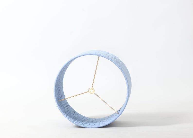 Puede incluir: Pantalla de l&aacute;mpara azul claro con forma cil&iacute;ndrica. La pantalla est&aacute; hecha de un material tejido y tiene una estructura met&aacute;lica de color lat&oacute;n. Dise&ntilde;ada para usarse con una base de l&aacute;mpara, es adecuada para varios estilos de decoraci&oacute;n.