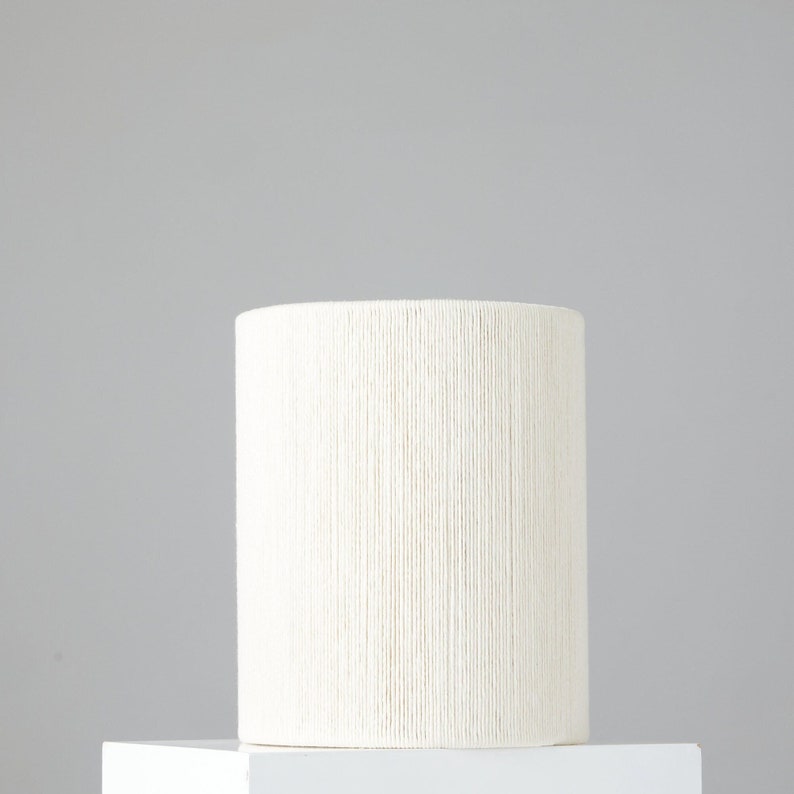 May include: A white cylindrical planter with a woven texture. The planter is made of a natural material and has a simple, modern design.