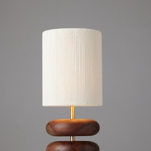 May include: A table lamp with a white linen shade and a wooden base. The base is made of two stacked, rounded pieces of wood.