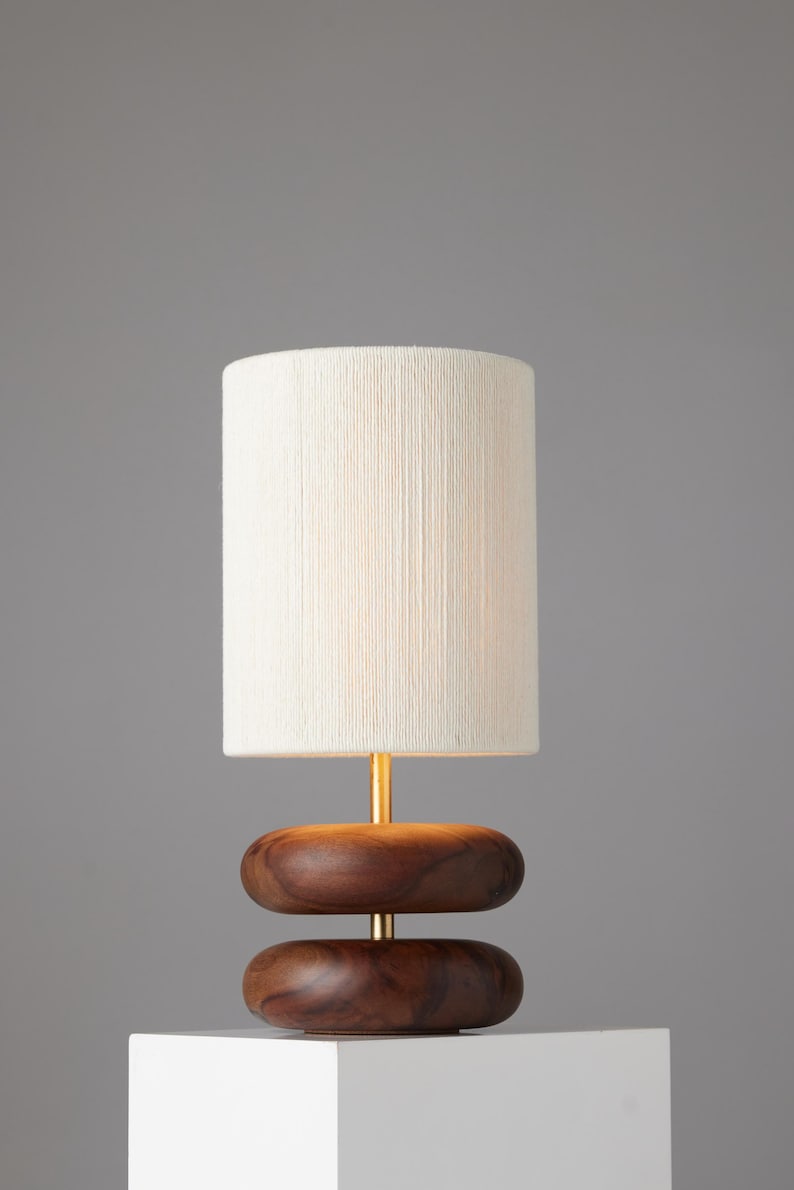 May include: A table lamp with a white linen shade and a wooden base. The base is made of two stacked, rounded pieces of wood.