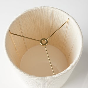 May include: A white lampshade made of woven rope with a gold metal frame.