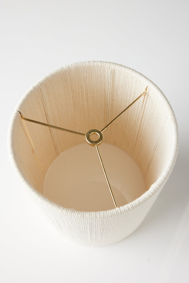 May include: A white lampshade made of woven rope with a gold metal frame.