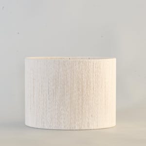 Puede incluir: Pantalla de l&aacute;mpara cil&iacute;ndrica con superficie texturizada blanquecina. La pantalla presenta un patr&oacute;n lineal vertical y est&aacute; dise&ntilde;ada para colocarse sobre una base de l&aacute;mpara. El color neutro y el dise&ntilde;o sencillo la hacen adecuada para varios estilos de interior.