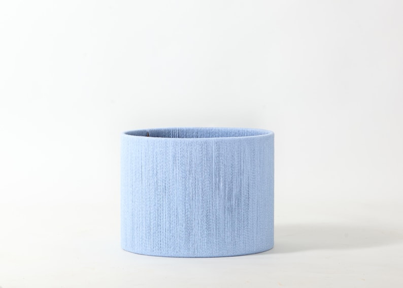 Puede incluir: Pantalla de l&aacute;mpara cil&iacute;ndrica azul claro. La superficie texturizada presenta l&iacute;neas verticales, creando un patr&oacute;n sutil. El dise&ntilde;o es simple y elegante, adecuado para varios estilos de decoraci&oacute;n de interiores. Medidas en cent&iacute;metros.