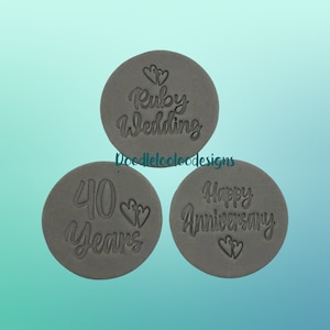 May include: Three grey, circular tokens with embossed text. One says "Ruby Wedding" with two hearts, another reads "40 Years" with two hearts, and the last says "Happy Anniversary" with two hearts. The tokens are arranged on a gradient blue background.