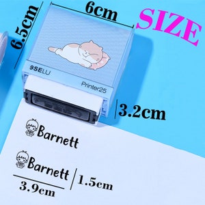 May include: A blue self-inking stamp with a cat design and the text "Printer25". The stamp measures 6 cm by 6.5 cm and has a 3.2 cm ink pad. The stamp is used to create a personalised signature with the name "Barnett" and a small cartoon boy.