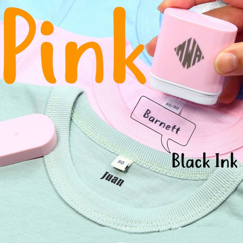 May include: A pink fabric label maker with a black ink cartridge. The label maker is being used to label a pink shirt with the name "Barnett" and a green shirt with the name "Juan".