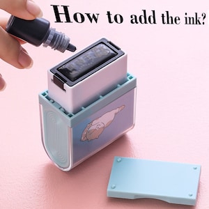 May include: A blue and white stamp with a cartoon cat design. The stamp is open and a small bottle of black ink is being used to refill the ink pad.