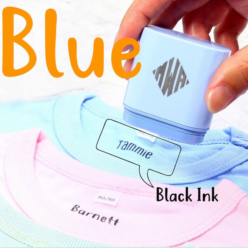 May include: A blue fabric label maker with a white logo and the word "MWA" printed on it. The label maker is being used to label a light blue t-shirt with the name "Tammie" in black ink. The t-shirt is on top of a pink t-shirt with the name "Barnett" labeled in black ink.
