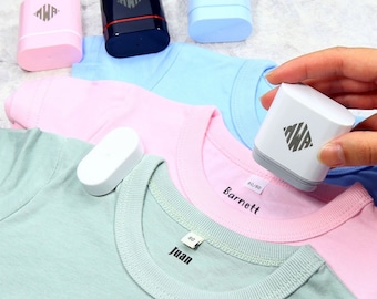 May include: Four different colored ink pads with the letters "MWA" in a diamond shape on the top. The ink pads are on top of three different colored t-shirts. The t-shirts have the names "Juan", "Barnett" and "80/80" written on them.
