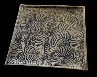 May include: A square tray with a black and white zebra print design. The tray is made of a light brown material and has a slightly raised edge.