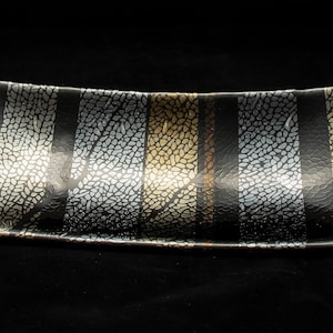 May include: A black glass serving tray with a wavy edge and a decorative pattern of silver and gold leaf. The pattern resembles a tree branch with leaves.